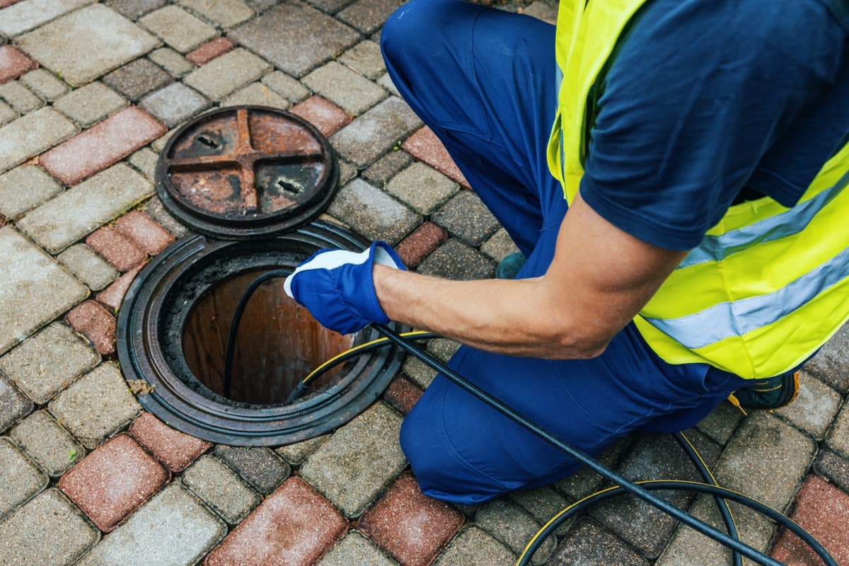 A drain technician guiding an inspection cable into an access opening